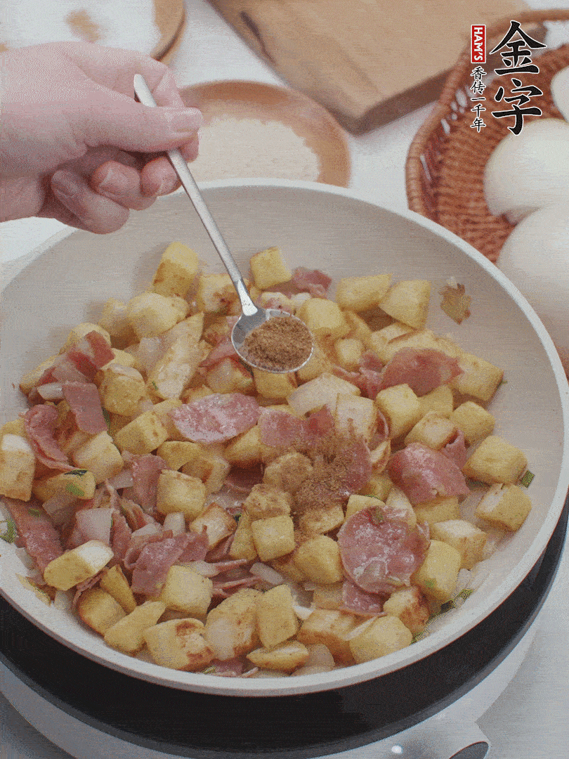 起鍋少油，煸香洋蔥丁、蔥白，加入金字培根火腿翻炒幾下，再加入饅頭丁、1小勺孜然粉、少許鹽翻炒均勻并鋪平。